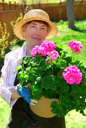Smiling senior woman holding a pot with flowers in her garden