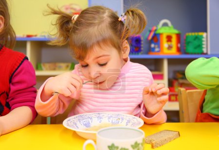 Little girl eats in kindergarten