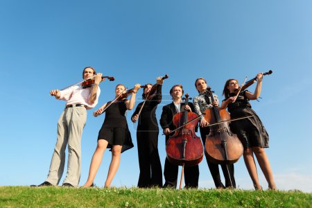 Six musicians play violins against sky
