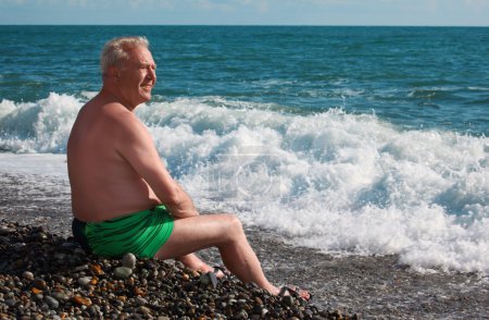 Elderly man sits on seacoast