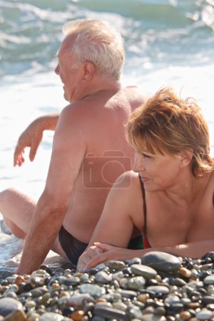 Aged pair sit on pebble beach
