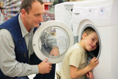 Man looks at washing machine in store, boy glances inward it