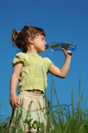 Girl standing in grass drinks water from plastic bottle