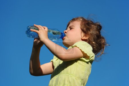 Girl drinks water from plastic bottle against blue sky