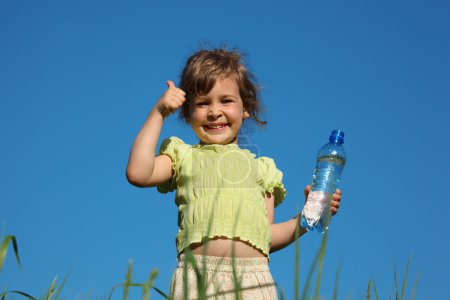 Girl in grass with plastic bottle with water shows gesture by fi