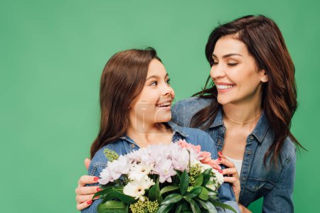 beautiful mother embracing daughter with flower bouquet isolated on green