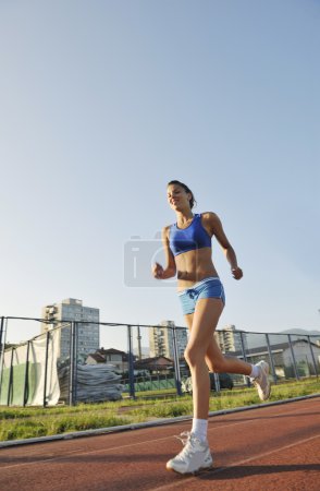 Beautiful young woman exercise jogging and runing on athletic track on stadium at sunrise