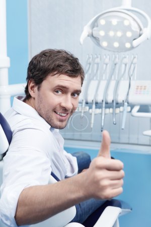 A young man in a dental chair shows thumbs up