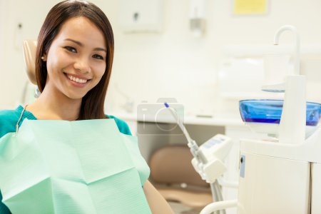 smiling asian woman sitting at the dentist and smiles towards th