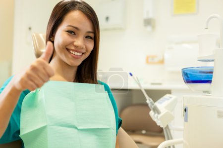 smiling asian woman sitting at the dentist and smiles towards th