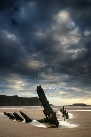 Landscape image of old shipwreck on beach at sunset in Summer