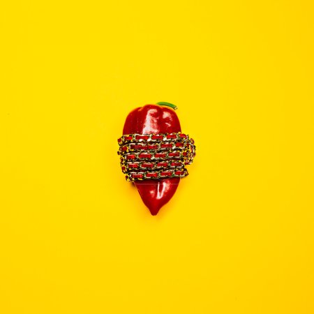 Conceptual fashion photography. Bright red pepper wrapped gold chain on a yellow background.