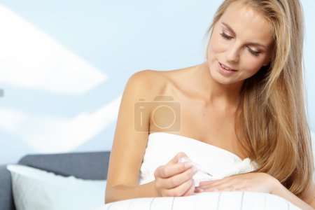 Woman applying nail polish in bed