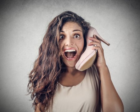 Excited girl talking on the phone, using a high-heeled shoe