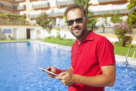 Man using a tablet at the poolside.