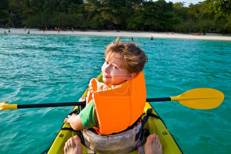 Boy paddles in a canoe at the ocean with safety west