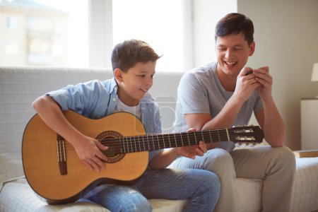 Boy playing guitar with father