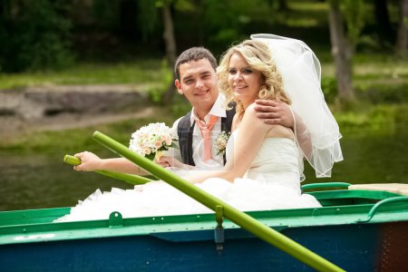 smiling bride and groom riding on rowing boat on lake