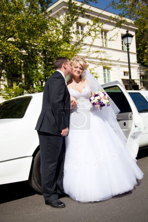 Groom kissing bride in cheek against white limousine