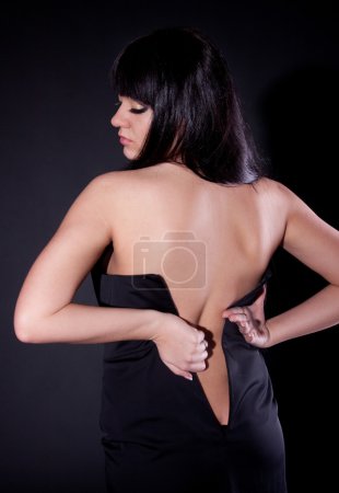 Portrait from back of overweighted woman trying to put on dress