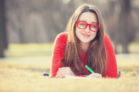 Teen girl with a pen lying down on a grass.
