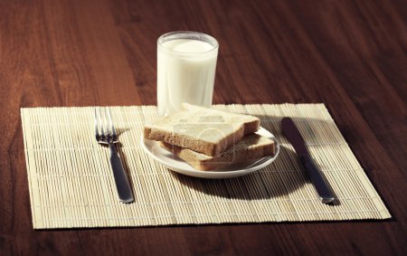 Toast with a glass of milk and knife on wooden background
