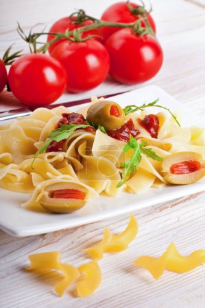 Pasta with tomato and arugula on the wooden table