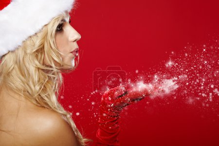pretty young brunette woman dressed as Santa blowing on the snow