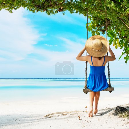 Woman in blue dress swinging at beach