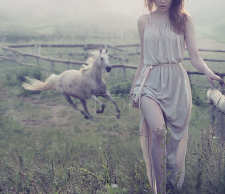 Delicate brunette posing with horse in the background