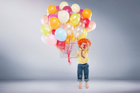 Small jumping boy holding bunch of balloons