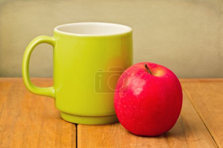 Red apple and green cup on wooden table