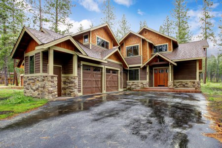 Large mountain cabin house with stone and wet driveway.