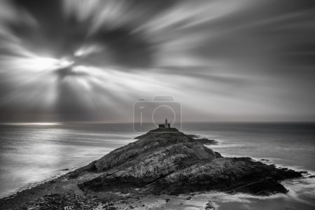 Lighthouse on headland with sun beams over ocean landscape with 