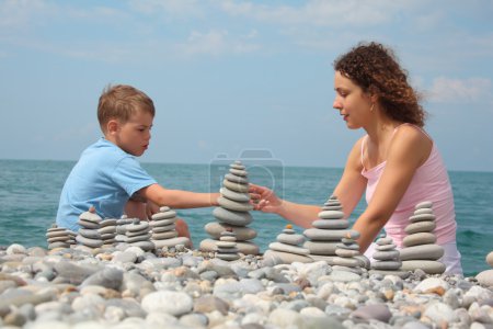 Mother and son builds stone stacks on pebble beach
