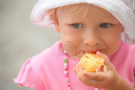 Little girl is eating orange