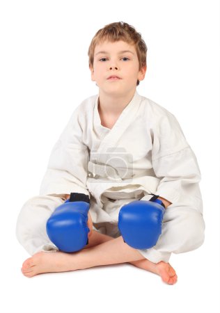 Little boxer boy in white dress and blue boxing gloves sitting i