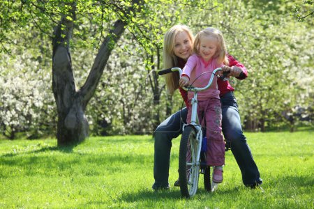 Girl with mother sit on bicycle in blossoming spring garden