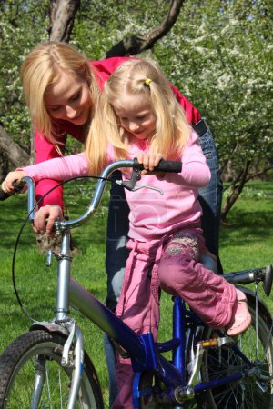 Mother learns daughter to go by bicycle in spring garden