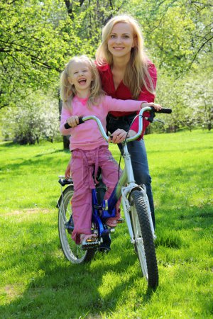 Laughing girl on bicycle with mother in spring garden