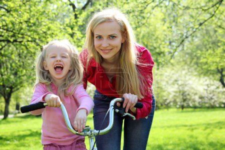 Laughing girl on bicycle with mother in spring garden