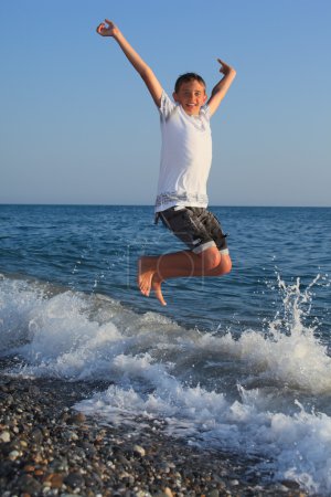 Jumping teenager boy on stone seacoast