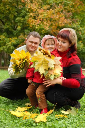Married couple and little girl collect maple leaves In park in a