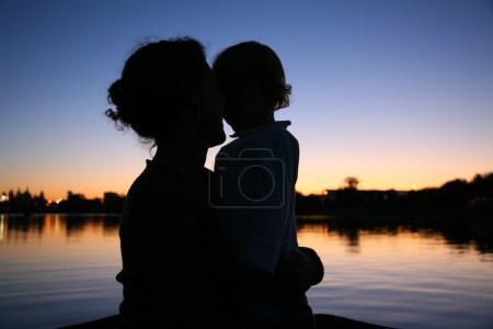 The silhouette of mother with the child against the background of the sunse