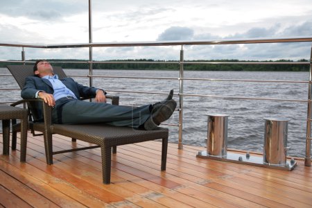 Portrait of man, who rests in chaise lounge on wharf near water