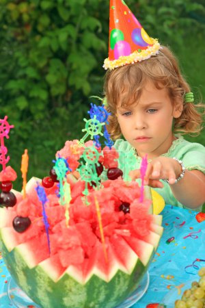 Little girl in cap eats fruit in garden, happy birthday