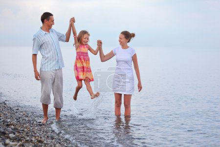 Happy family with little girl on beach in evening, parents lift