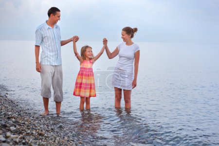 Happy family with little girl walk on beach in evening, having j