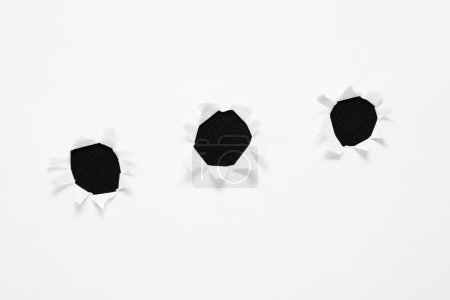 The sheet of paper with the three torn holes against the black background