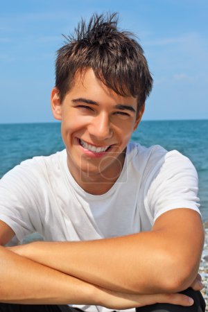 Smiling teenager boy against sea, Looking at camera